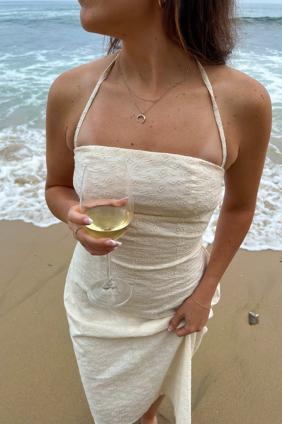Model posing at the beach holding a wine glass.